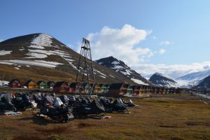 Blick in ein Tal mit drei Gipfeln, Schneemobile ohne Schne, spitze, bunte Häuser