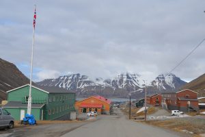 Straße, die bergab führt, bunte Häuser, im Hintergrund Fjord und Berge