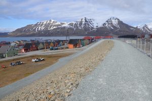 Blick über einen Wall, im Hintergrund Häuser, Fjord Berge