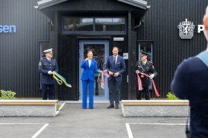 scharzes Gebäude, Frau in hellbauem Hosenanzug, Mann in dunkelblauem Anzug, zwei Polizisten, Band in schwedischen und norwegischen Farben