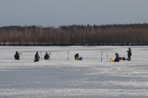 Leute sitzen auf dem Eis, neben sich Eisbohrer